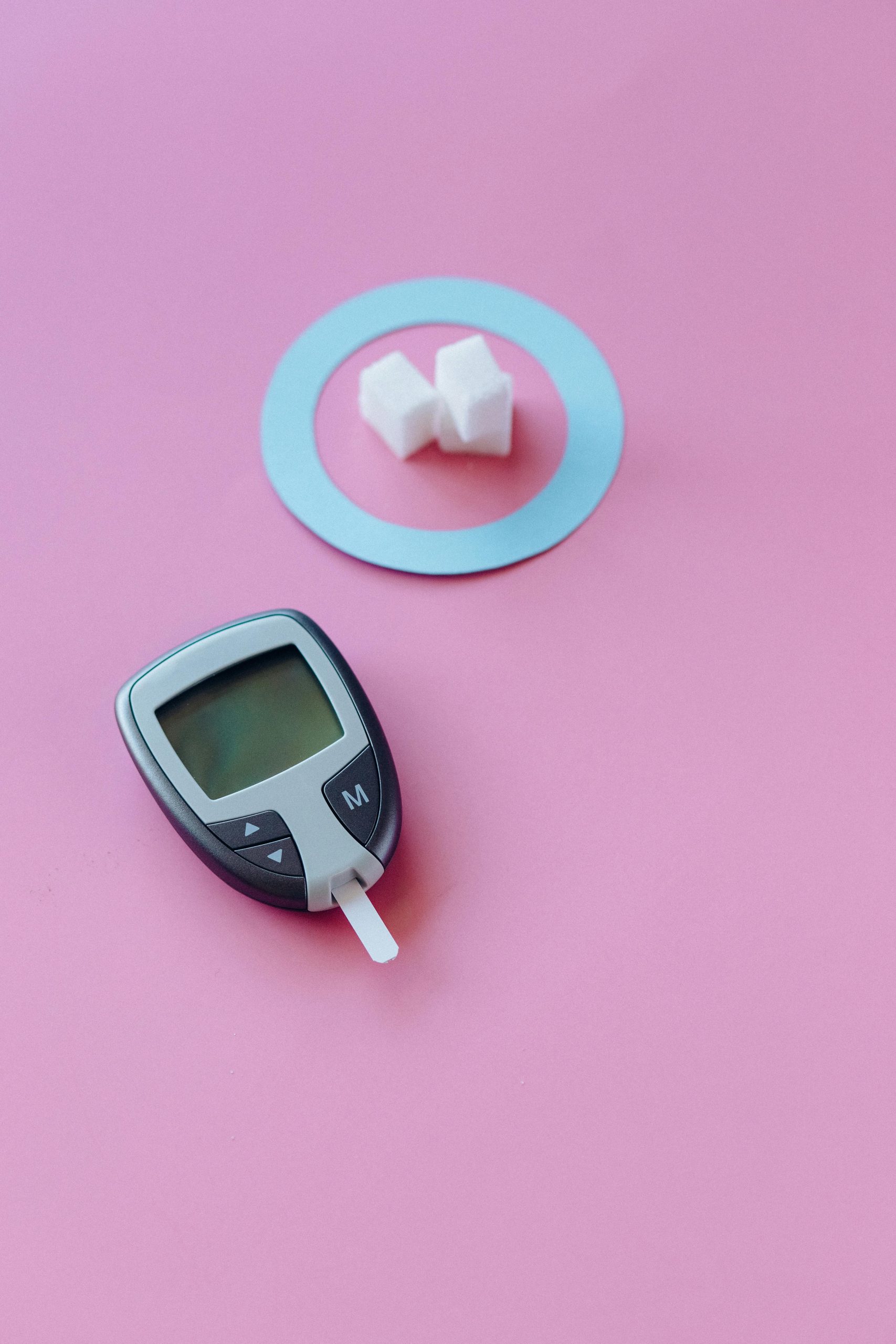 Glucometer device and sugar cubes on a pink background symbolizing diabetes awareness.